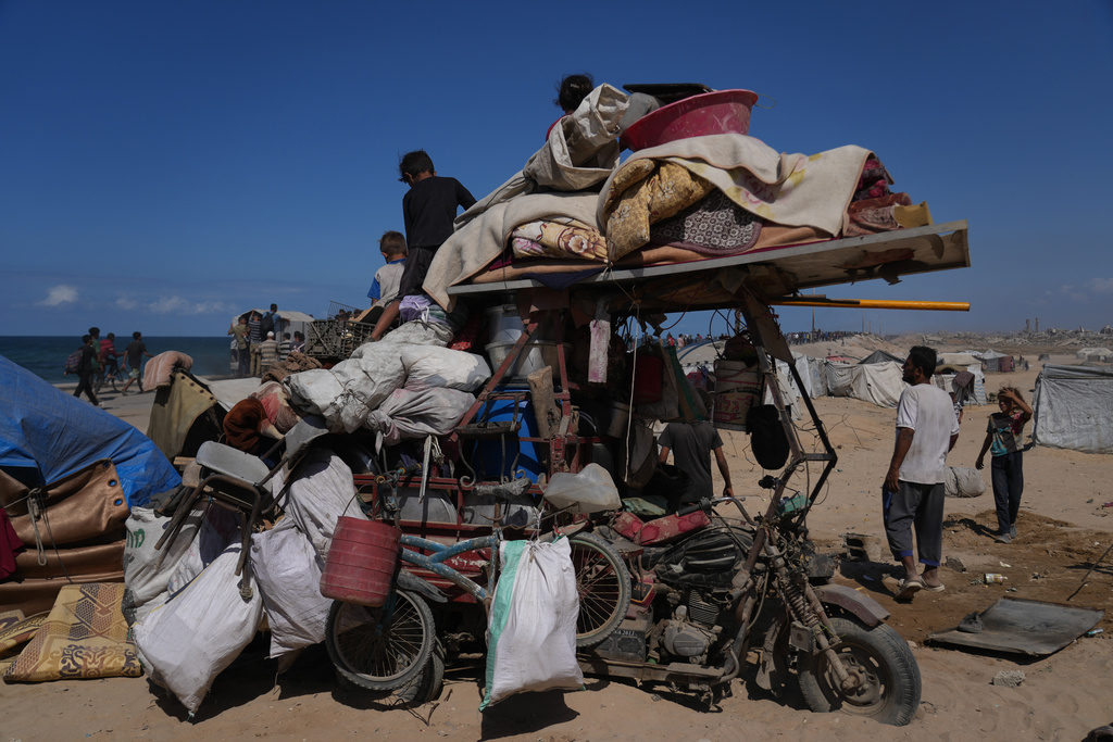 Displaced Palestinians sit and stand next to their belongings piled on a motorcycle near Wadi Gaza in the central Gaza Strip, Friday, Oct. 10, 2025, after Israel and Hamas agreed to a pause in their war and the release of the remaining hostages. (AP Photo/Abdel Kareem Hana)