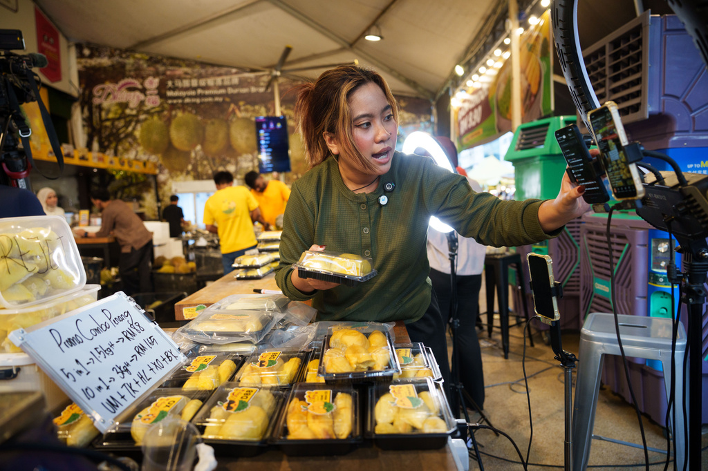 A worker livestreams while selling durians at a durian stall in Petaling Jaya, on the outskirts of Kuala Lumpur, Malaysia, Monday, June 22, 2026. (AP Photo/Vincent Thian)