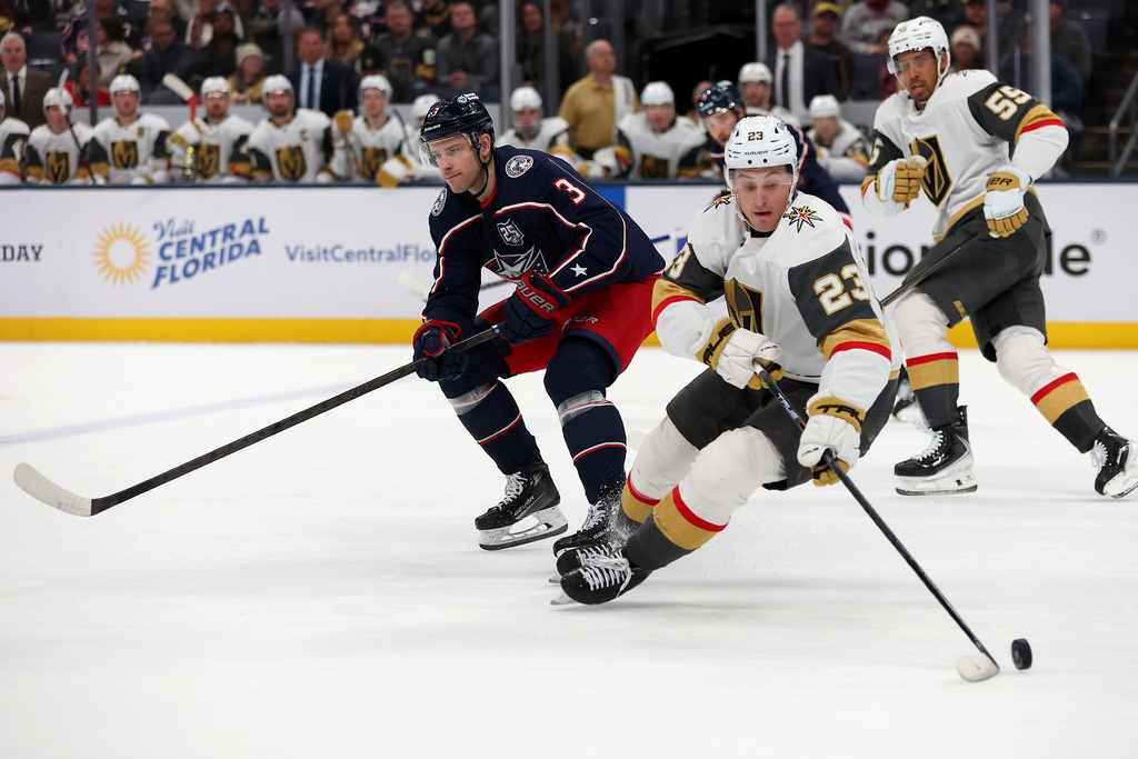 Vegas Golden Knights left wing Cole Reinhardt (23) controls the puck as Columbus Blue Jackets center Charlie Coyle (3) skates past during the first period of an NHL hockey game, Saturday, Dec. 13, 2025, in Columbus, Ohio. (AP Photo/Joe Maiorana)