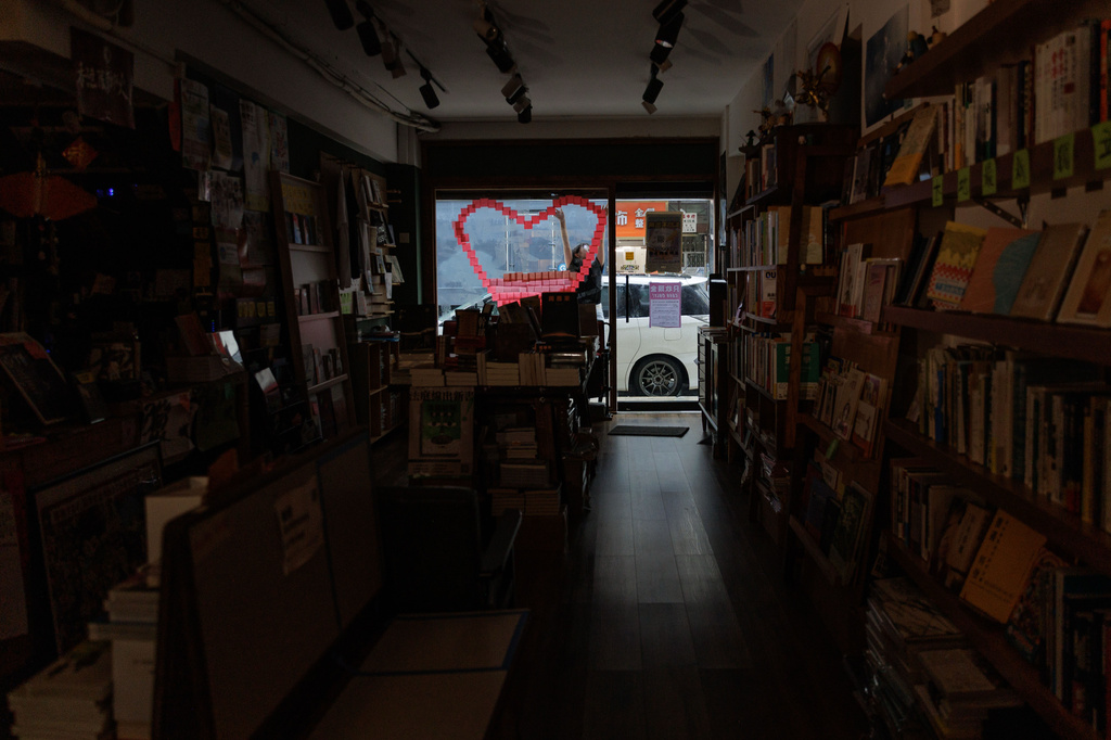 A staff member opens Hunter Bookstore at noon near a heart-shaped display on the front window in Hong Kong, Friday, Aug. 14, 2026. (AP Photo/May James)