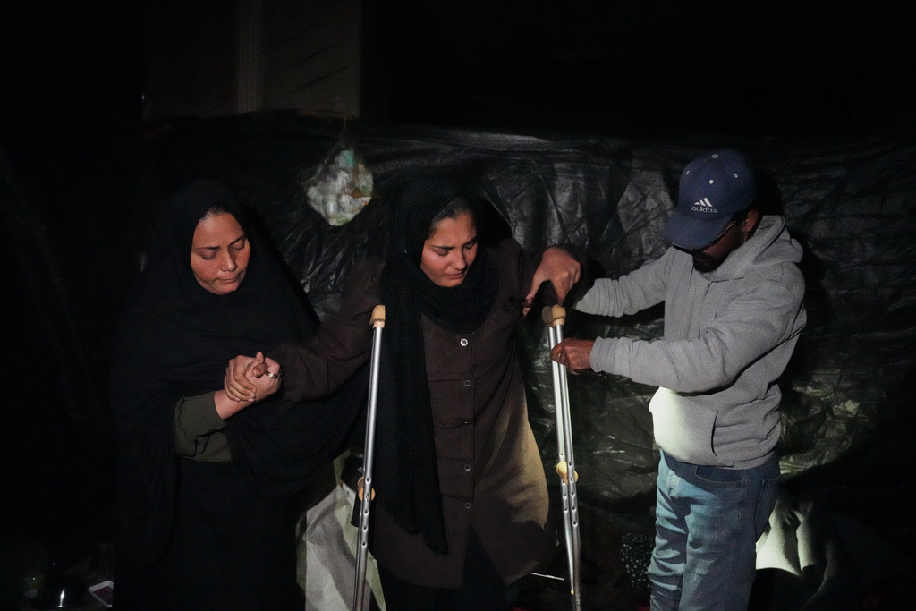 Rimas Abu Lehia, 15, who was injured in her left leg by Israeli fire, tries to sit on the ground with the help of her parents inside her family's tent in Khan Younis, Gaza Strip, Tuesday, Jan. 27, 2026, as she awaits permission to travel outside Gaza for medical treatment. (AP Photo/Abdel Kareem Hana)