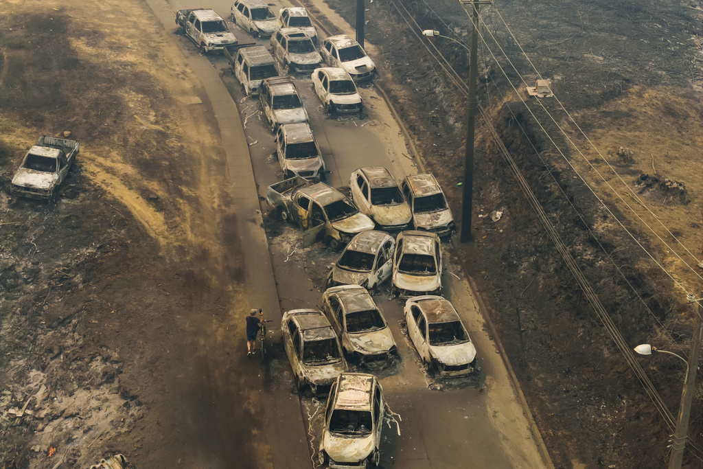 Damaged vehicles line a road after wildfires swept through residential areas in Lirquen, Chile, Sunday, Jan. 18, 2026. (AP Photo/Javier Torres)