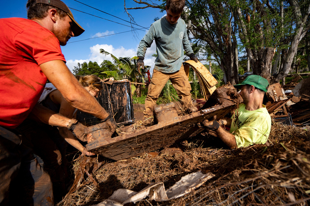 Residents Kaybri Jones, left, and Anthony Scala, and volunteers remove mud-covered debris at a temporary dump site, Tuesday, March 24, 2026, in Haleiwa, Hawaii. (AP Photo/Mengshin Lin)
