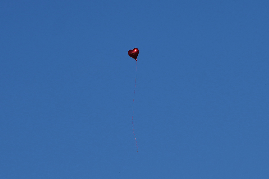 A heart shaped balloon files above people observing 16 minutes of silence in memory of the victims, outside the train station on the first anniversary of the disaster that killed 16 people, in Novi Sad, Serbia, Saturday, Nov. 1, 2025. (AP Photo/Darko Vojinovic)