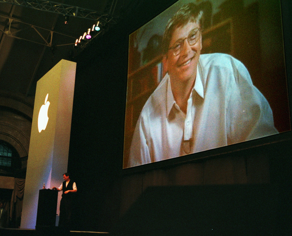 FILE - Apple Computer Inc. co-founder and current adviser Steve Jobs, background left, stands at a podium as Bill Gates, chief executive of Microsoft Corp., appears on a video screen as he addresses the MacWorld convention praising the new alliance between Apple and Microsoft Wednesday, Aug. 6, 1997, in Boston. (AP Photo/Julia Malakie, File)