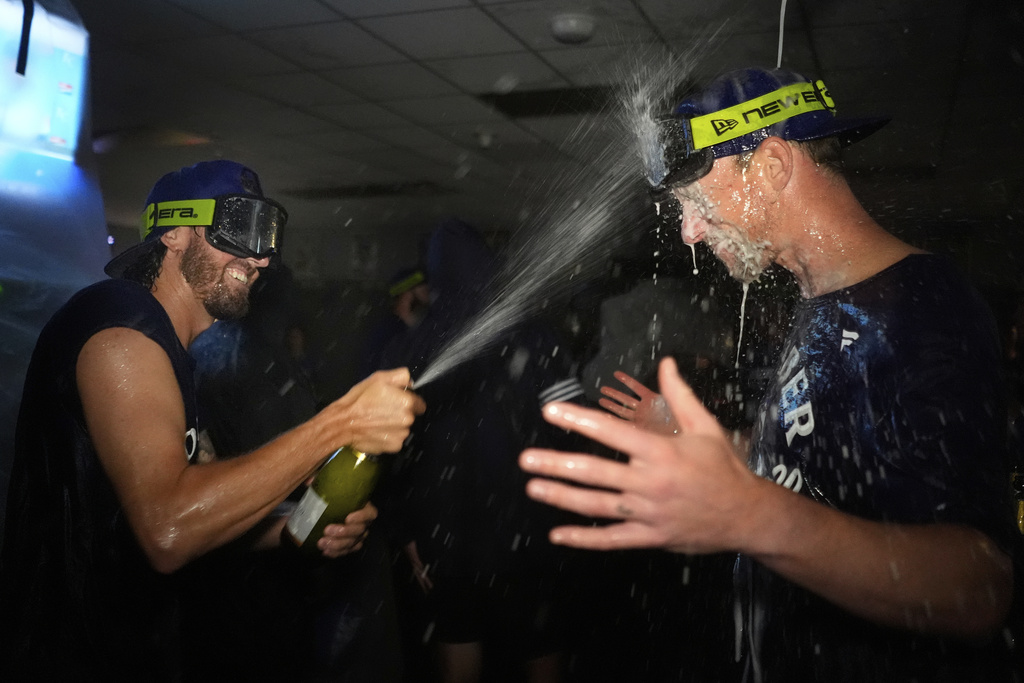 Toronto Blue Jays' Kevin Gausman, left, celebrates with Chris Bassitt in the clubhouse after their baseball game against the Kansas City Royals, Sunday, Sept. 21, 2025, in Kansas City, Mo. (AP Photo/Charlie Riedel)