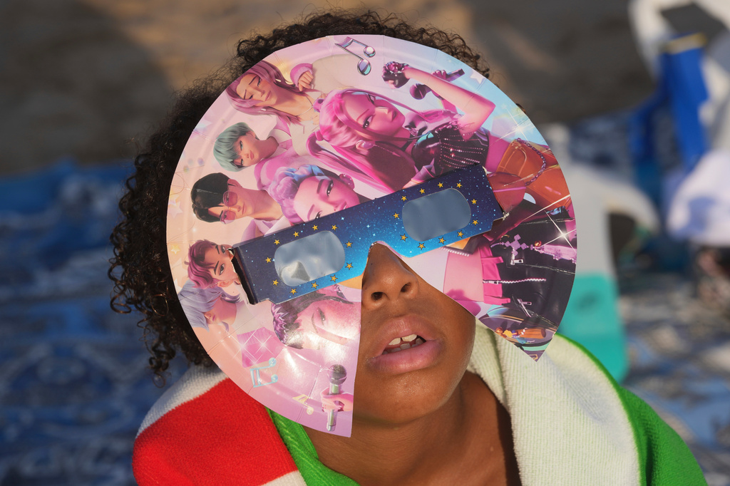 A beachgoer wearing special eclipse glasses looks up during the beginning phase of a solar eclipse at Puerto de Sagunto beach near Valencia, Spain, Wednesday, Aug. 12, 2026. (AP Photo/Alberto Saiz)