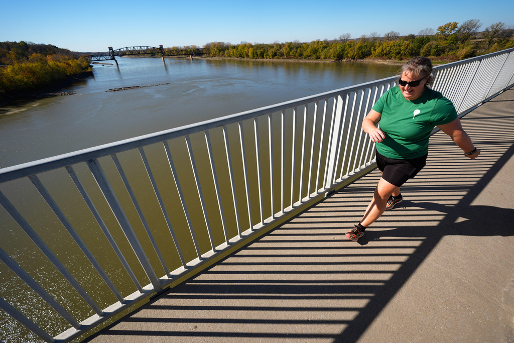 Stephanie Schuster crosses the Missouri River on a new bridge while the Katy railroad bridge rises in the distance Wednesday, Nov. 5, 2025, in Boonville, Mo. (AP Photo/Charlie Riedel)