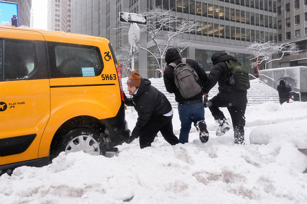 Cameron Betz helps push a taxi stuck in the snow during a snow storm, Monday, Feb. 23, 2026, in New York. (AP Photo/Seth Wenig)