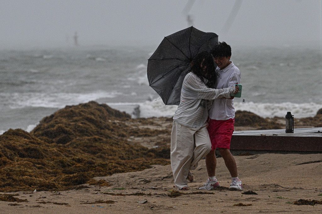 In this photo released by Xinhua News Agency, a tourist couple brace themselves against strong wind and rain at Tanmen central fishing port in Qionghai, south China's Hainan Province on Friday, July 3, 2026, as a severe weather system was affecting the area. (Pu Xiaoxu/Xinhua via AP)