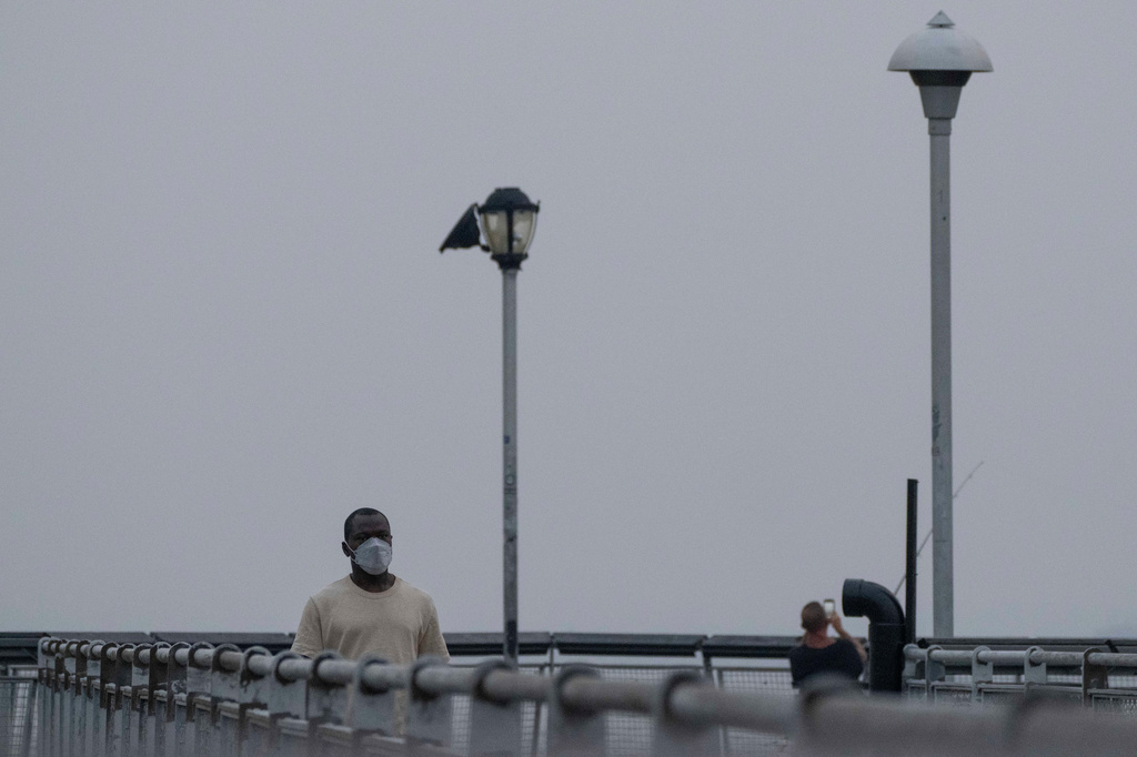A person wearing a mask walks on a pier as smoke from wildfires blankets the sky, Thursday, July 16, 2026, in the Brooklyn borough of New York. (AP Photo/Yuki Iwamura)