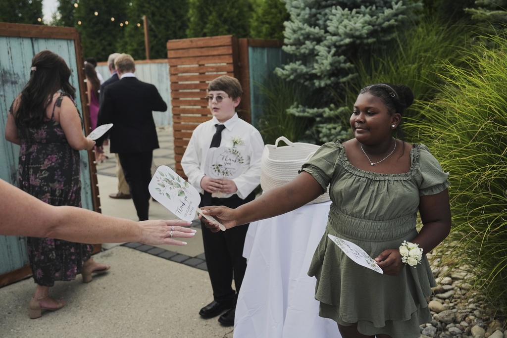 Zuri Jones, right, hands a fan to a guest as they arrive for a wedding Saturday, Aug. 23, 2025, in Newtown, Ohio. (AP Photo/Joshua A. Bickel)