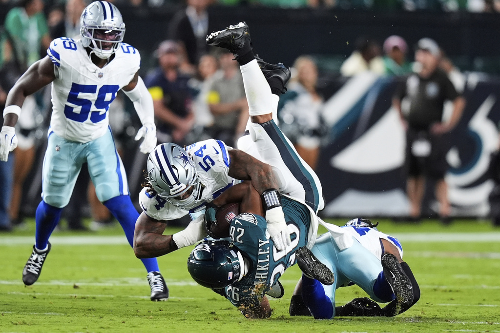 Philadelphia Eagles running back Saquon Barkley (26) is stopped after a gain by Dallas Cowboys' Sam Williams, top, and Malik Hooker, bottom, in the first half of an NFL football game Thursday, Sept. 4, 2025, in Philadelphia.(AP Photo/Chris Szagola)