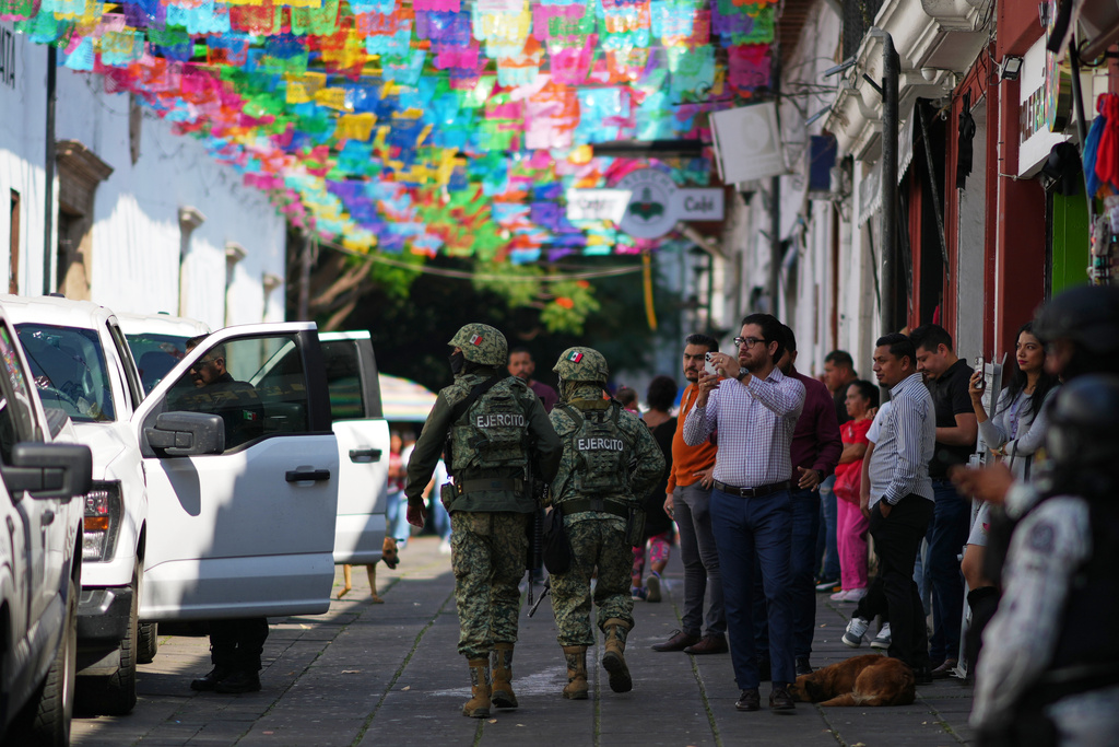 Soldiers patrol and pedestrians watch as Michoacan state prosecutor officers escort a suspect in the killing of the town's Mayor Carlos Manzo Rodriguez in Uruapan, Mexico, Friday, Nov. 21, 2025. (AP Photo/Eduardo Verdugo)
