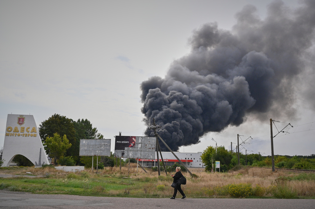 A woman walks by the burning warehouse at the city entrance following Russian air attack in Odesa, Ukraine, Sunday, Sept. 13, 2026. (AP Photo/Michael Shtekel)