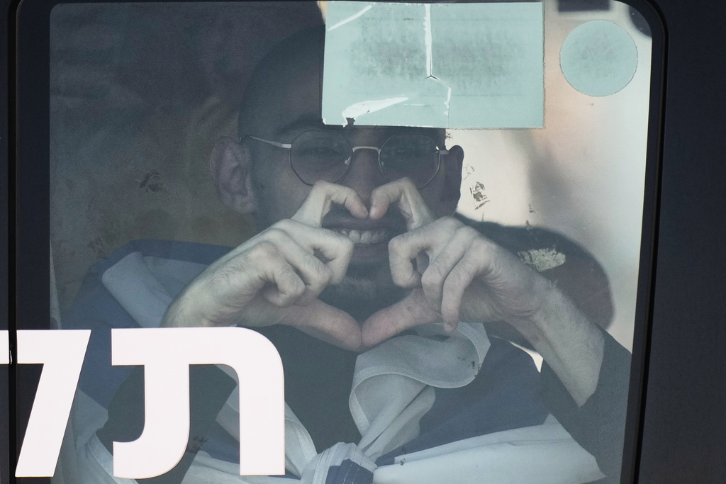 Rom Breslavski, an Israeli hostage released from the Gaza Strip smiles making a heart sign from a minibus at the Sheba Medical Center in Ramat Gan, Israel, Monday, Oct. 13, 2025. (AP Photo/Leo Correa)