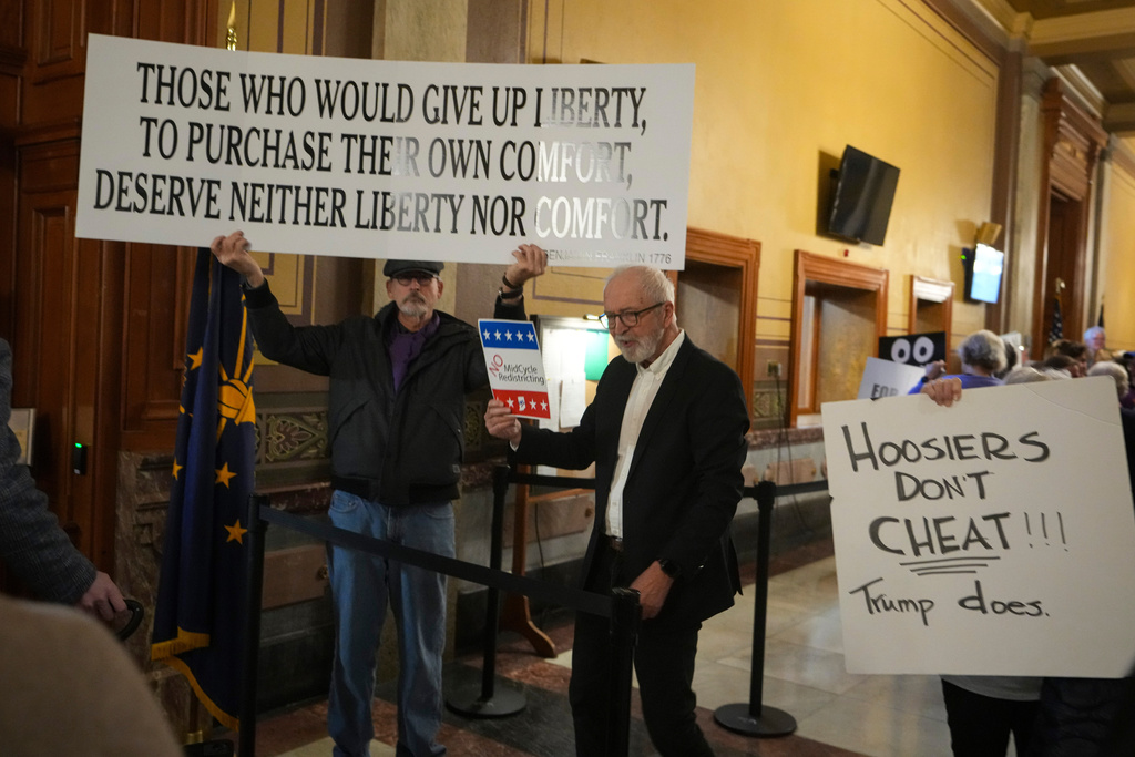 Protestors hold signs outside the Indiana Senate chamber before a vote to redistrict the state's congressional map at the Statehouse in Indianapolis, Thursday, Dec. 11, 2025. (AP Photo/Michael Conroy)