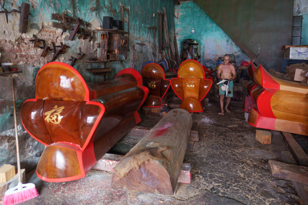 Traditional Chinese coffin maker Goh Khuay Par holds a cat and walks past completed Mei Hua coffins awaiting delivery at his workshop in Muar, Malaysia, Tuesday, July 14, 2026. (AP Photo/Vincent Thian)
