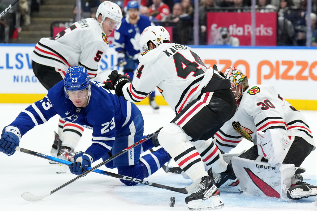 Toronto Maple Leafs forward Matthew Knies (23) gets knocked down by Chicago Blackhawks defenceman Wyatt Kaiser (44) as teammate Spencer Knight (30) makes the save during second period NHL hockey action in Toronto, Tuesday, Dec. 16, 2025. (Nathan Denette/The Canadian Press via AP)