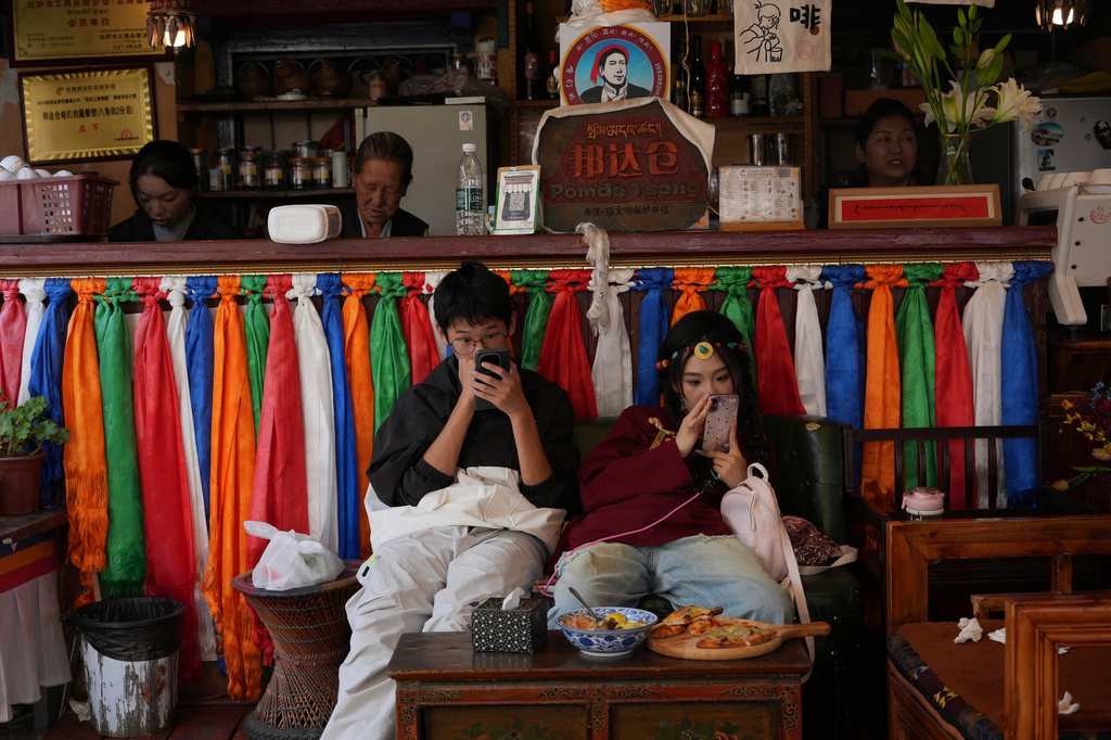 Tourists looks at their phones at a cafe in Pangdatsang Compound in Lhasa in western China's Tibet Autonomous Region on Tuesday, July 21, 2026, as seen during a government organized visit for foreign journalists. (AP Photo/Ng Han Guan)