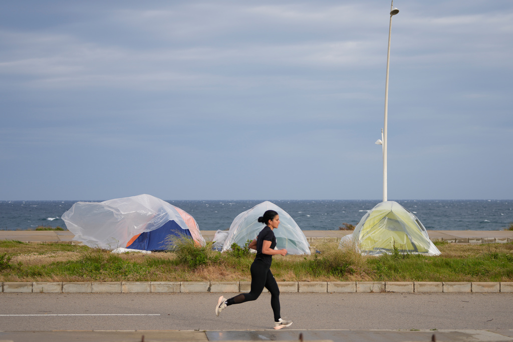 A woman runs past tents sheltering people displaced by Israeli airstrikes in southern Lebanon and Dahiyeh, Beirut's southern suburbs, along the Beirut waterfront in Beirut, Lebanon, Saturday, March 14, 2026. (AP Photo/Hassan Ammar)