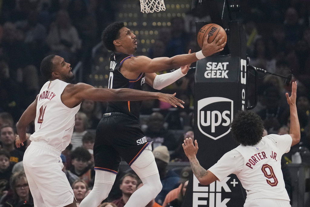 Phoenix Suns forward Ryan Dunn, center, shoots between Cleveland Cavaliers center Evan Mobley (4) and guard Craig Porter Jr. (9) in the first half of an NBA basketball game Wednesday, Dec. 31, 2025, in Cleveland. (AP Photo/Sue Ogrocki)