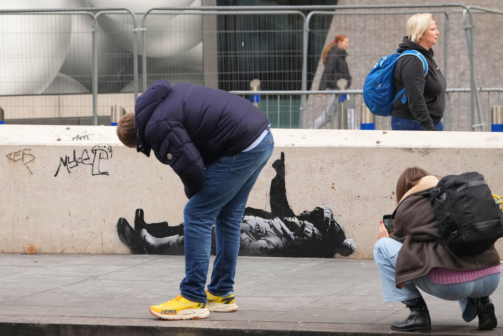 People take pictures of a graffiti artwork, depicting two people, outside Tottenham Court Road Station in London, Monday, Dec. 22, 2025 as elusive street artist Banksy appeared to confirm Monday that an identical image appeared on a wall on the side of a building in Bayswater, west London is his latest work. (AP Photo/Kirsty Wigglesworth)