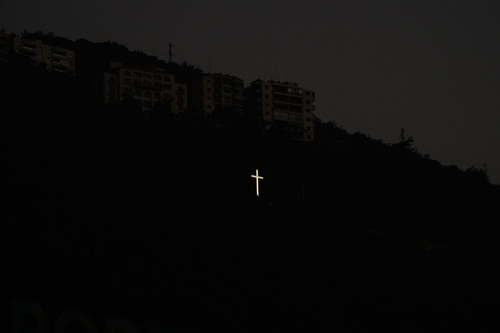A cross glows on a hillside above residential buildings at dusk in the coastal town of Jounieh, north of Beirut, Lebanon, Sunday, Nov. 9, 2025. (AP Photo/Hassan Ammar)