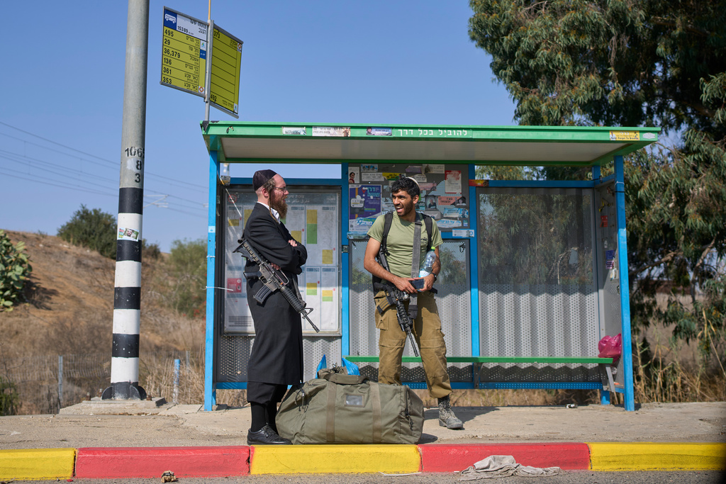 An Israeli soldier and an armed ultra-Orthodox Jewish man are seen at a bus stop in southern Israel, Tuesday, Nov. 18, 2025. (AP Photo/Ohad Zwigenberg)