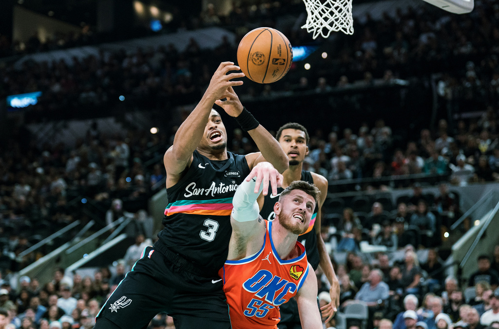 San Antonio Spurs forward Keldon Johnson (3) and Oklahoma Thunder center Isaiah Hartenstein (55) vie for a rebound during the first half of an NBA basketball game in San Antonio, Tuesday, Dec. 23, 2025. (AP Photo/Rodolfo Gonzalez)