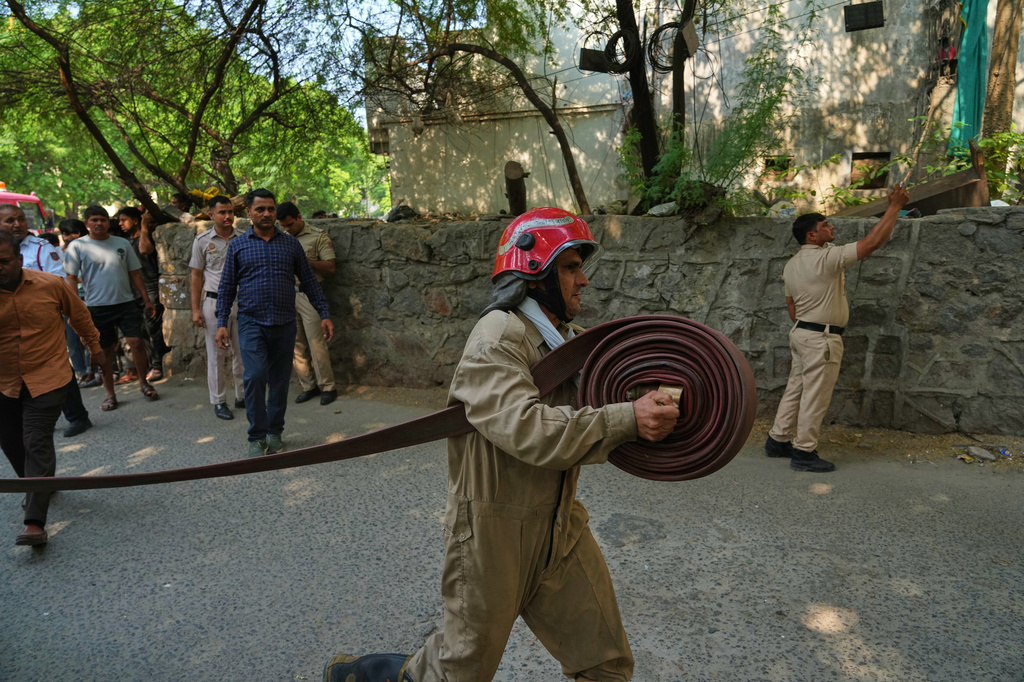 A firefighter runs with a hose toward a hotel fire in New Delhi, India, Wednesday, June 3, 2026. (AP Photo/Manish Swarup)