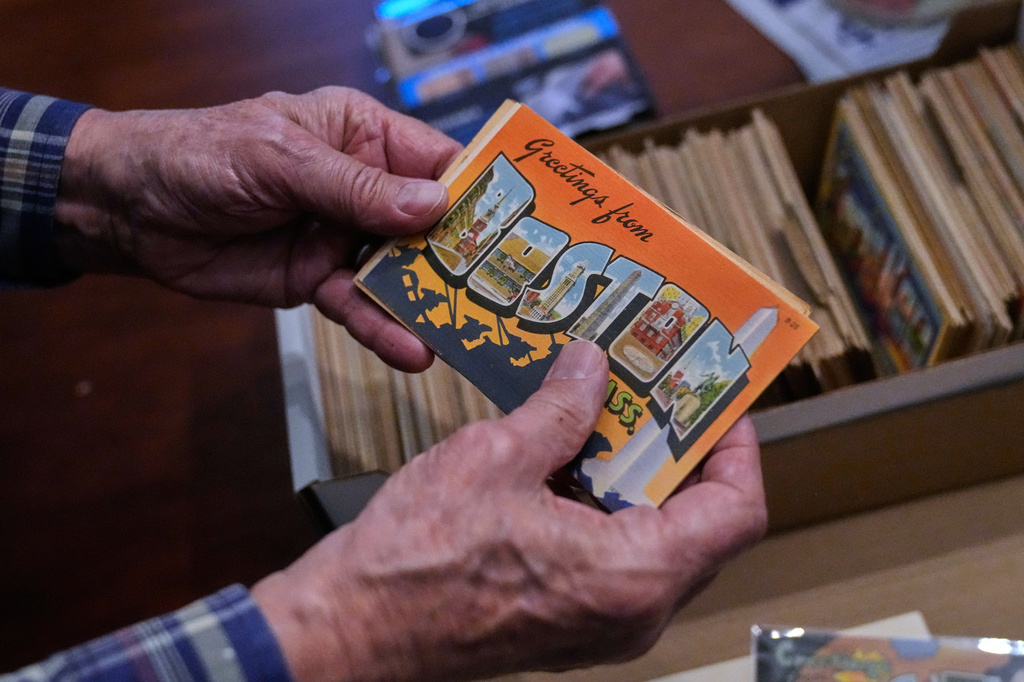 Peter Meggison, a 76-year-old retired community college professor, examines a "Greetings from Boston" postcard from his private collection of more than 10,000 large letter postcards, Monday, May 11, 2026, in Westport, Mass. (AP Photo/Charles Krupa)