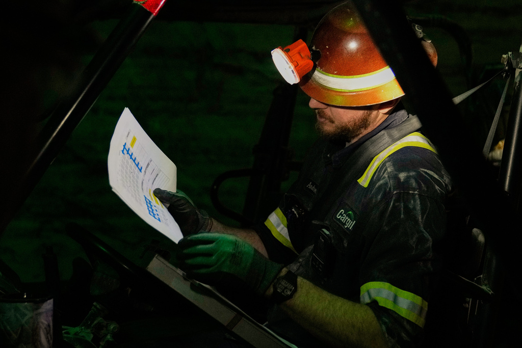 The absolute darkness of the mine is broken as supervisor Andrew Adkins uses a headlamp to lookover a map of drilling sites at the Cargill Salt Mine, 1,800 feet below the surface of Lake Erie, in Cleveland, Ohio, Thursday, March 19, 2026. (AP Photo/Sue Ogrocki)