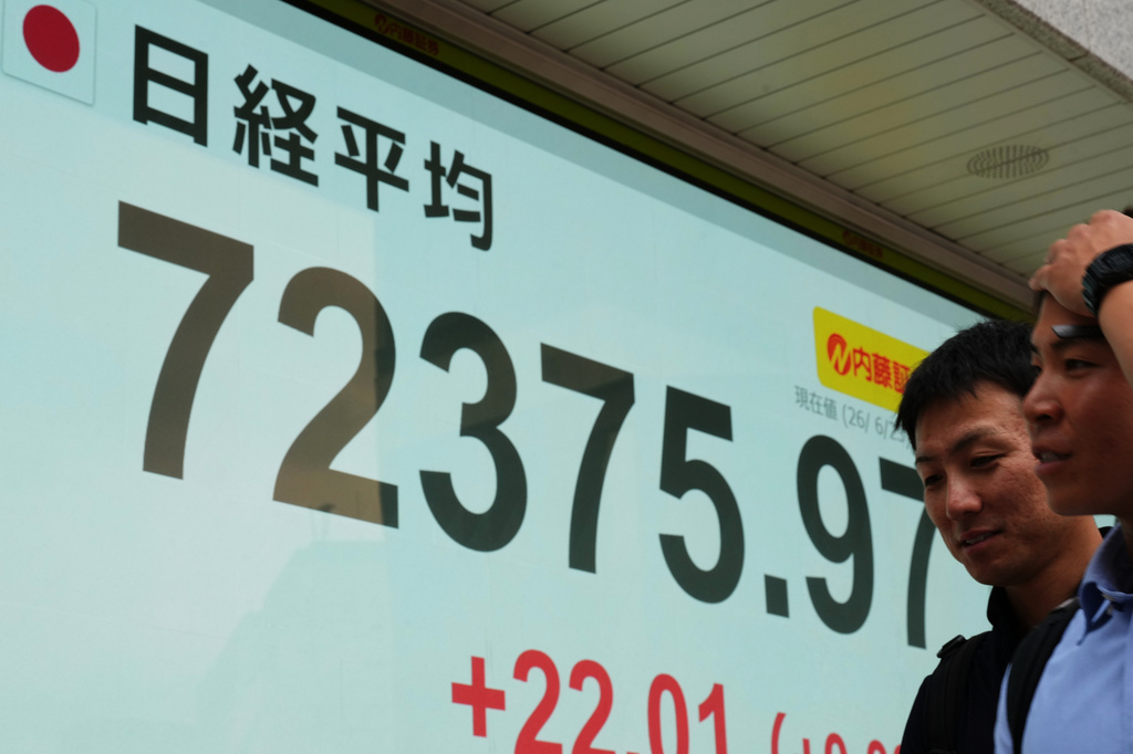 People walk past a monitor showing Japan's Nikkei 225 index at a securities firm in Tokyo, Tuesday, June 23, 2026. (AP Photo/Hiro Komae)