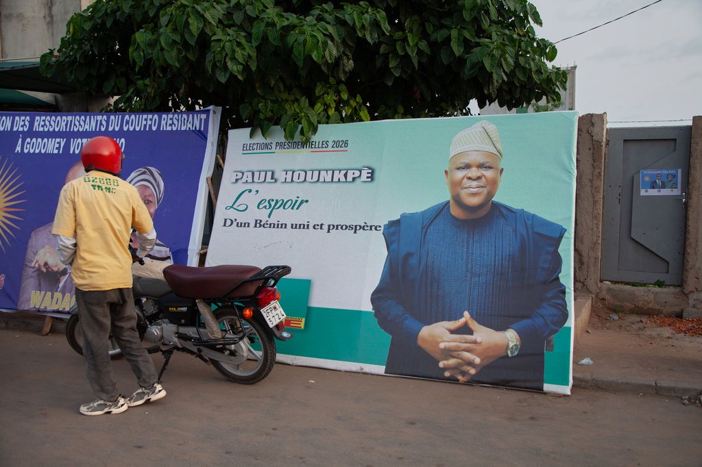 A motorcyclist stands beside a billboard featuring presidential candidate Paul Hounkpe in Cotonou, Benin, Friday, April 10, 2026. (AP Photo/Abadjaye Justin Sodogandji)