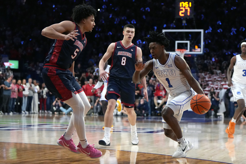 BYU guard Robert Wright III drives between Arizona guard Brayden Burries and forward Ivan Kharchenkov (8) during the first half of an NCAA college basketball game, Wednesday, Feb. 18, 2026, in Tucson, Ariz. (AP Photo/Rick Scuteri)