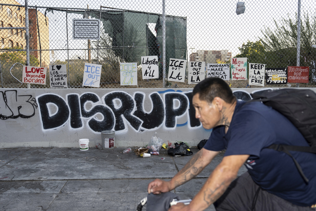 A man rides his bike past signs protesting ICE, displayed on a fence across the street from a Home Depot in Los Angeles, Tuesday, Aug. 5, 2025, amid ongoing ICE raids. (AP Photo/Jae C. Hong)