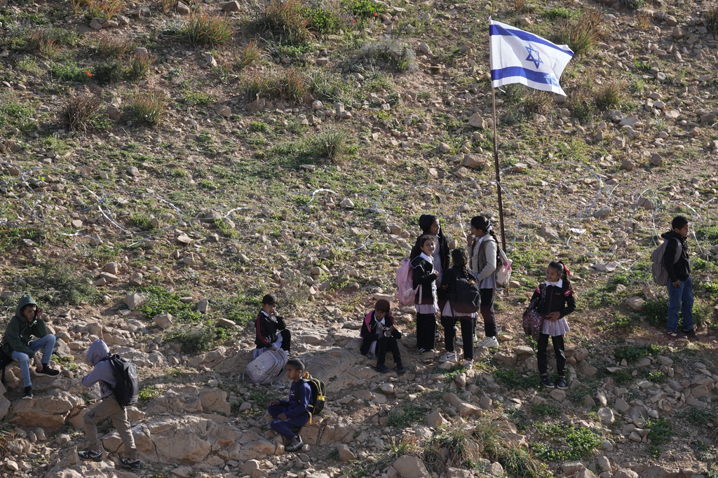 Palestinian students walk to school along a fence separating their village from a nearby Israeli settlement of Carmel, which forces them to take an alternative route nearly twice as long, near the West Bank village of Umm al-Khair, Tuesday, April 14, 2026. (AP Photo/Mahmoud Illean)
