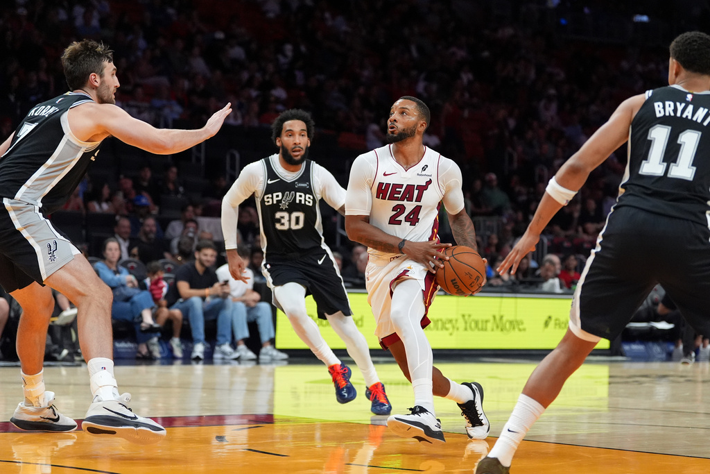 Miami Heat guard Norman Powell (24) drives forward through the defense of San Antonio Spurs forward Julian Champagnie (30), center/forward Luke Kornet (7) and forward Carter Bryant (11) during the second half of a preseason NBA basketball game, Wednesday, Oct. 8, 2025, in Miami. (AP Photo/Rebecca Blackwell)