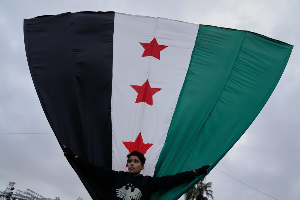 A Syrian man waves his country flag during celebrations marking the first anniversary of the ousting of former President Bashar Assad in Damascus, Syria, Monday, Dec. 8, 2025. (AP Photo/Hussein Malla)