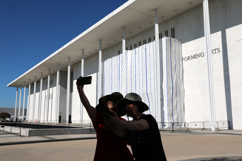 Women take a selfie as the wall of the John F. Kennedy Center for the Performing Arts is covered in tarp as work continues on the removal of President Donald Trump's name, Saturday, June 13, 2026 in Washington. (AP Photo/Rahmat Gul)