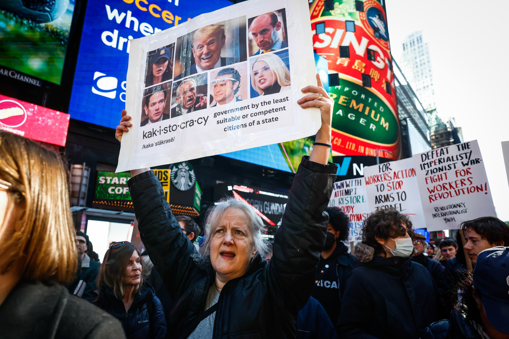 A woman holds up a placard with images of President Donald Trump and some of his cabinet members, during a protest against U.S. and Israeli strikes on Iran, in New York, Saturday, Feb. 28, 2026. (AP Photo/Kena Betancur)