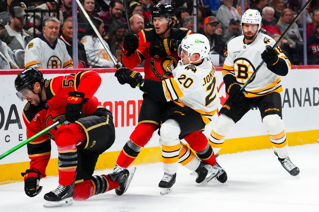Ottawa Senators' Ridly Greig, center, hits Boston Bruins' Henri Jokiharju (20) during second-period NHL hockey game action in Ottawa, Ontario, Monday, Oct. 27, 2025. (Sean Kilpatrick/The Canadian Press via AP)
