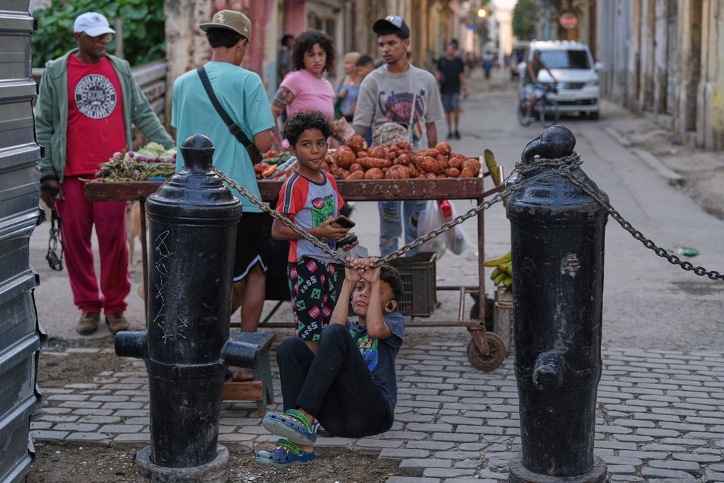 A child hangs on chains while customers shop at a street stall in Old Havana, Monday, January 5, 2026. (AP Photo/Ramon Espinosa)