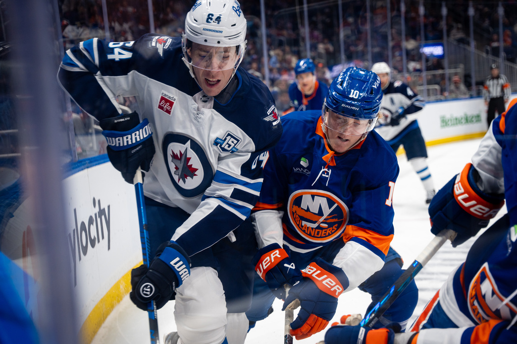 Winnipeg Jets defenseman Logan Stanley (64) and New York Islanders right wing Simon Holmstrom (10) fight for the puck during the second period of an NHL hockey game, Monday, Oct. 13, 2025, in Elmont, N.Y. (AP Photo/Angelina Katsanis)