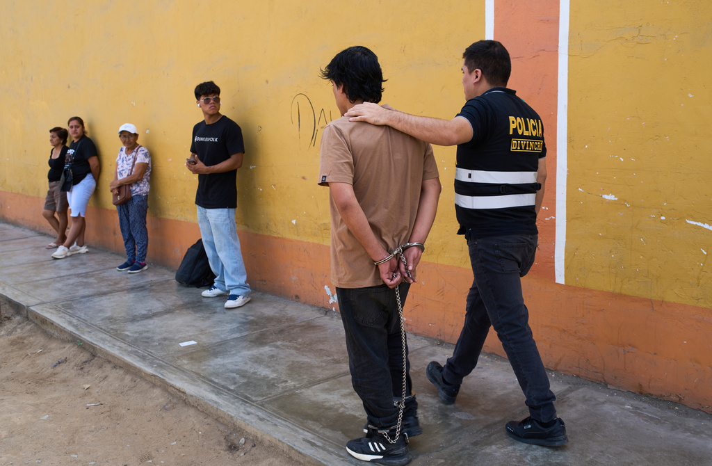 A police officer escorts a detainee accused of being part of a criminal gang after a news conference at a downtown police station in Trujillo, Peru, Thursday, May 21, 2026. (AP Photo/Rodrigo Abd)