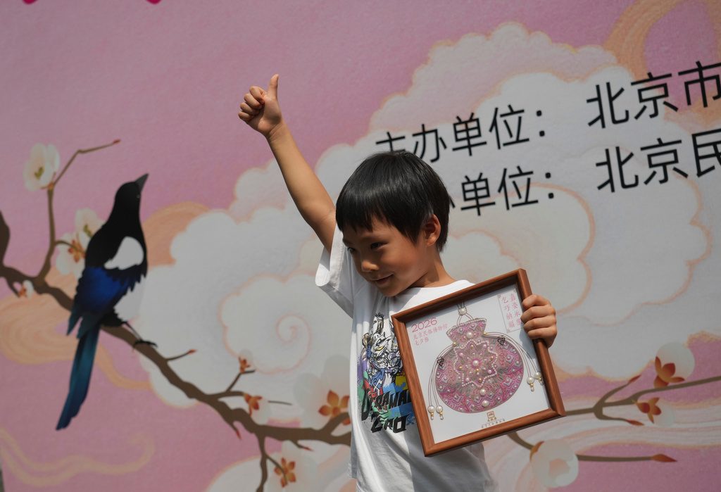 A child celebrates with his finished sachet-shaped Song brocade pearl painting during a festival to celebrate Qixi at the Beijing Folk Custom Museum in Beijing, Wednesday, Aug. 19, 2026. (AP Photo/Achmad Ibrahim)