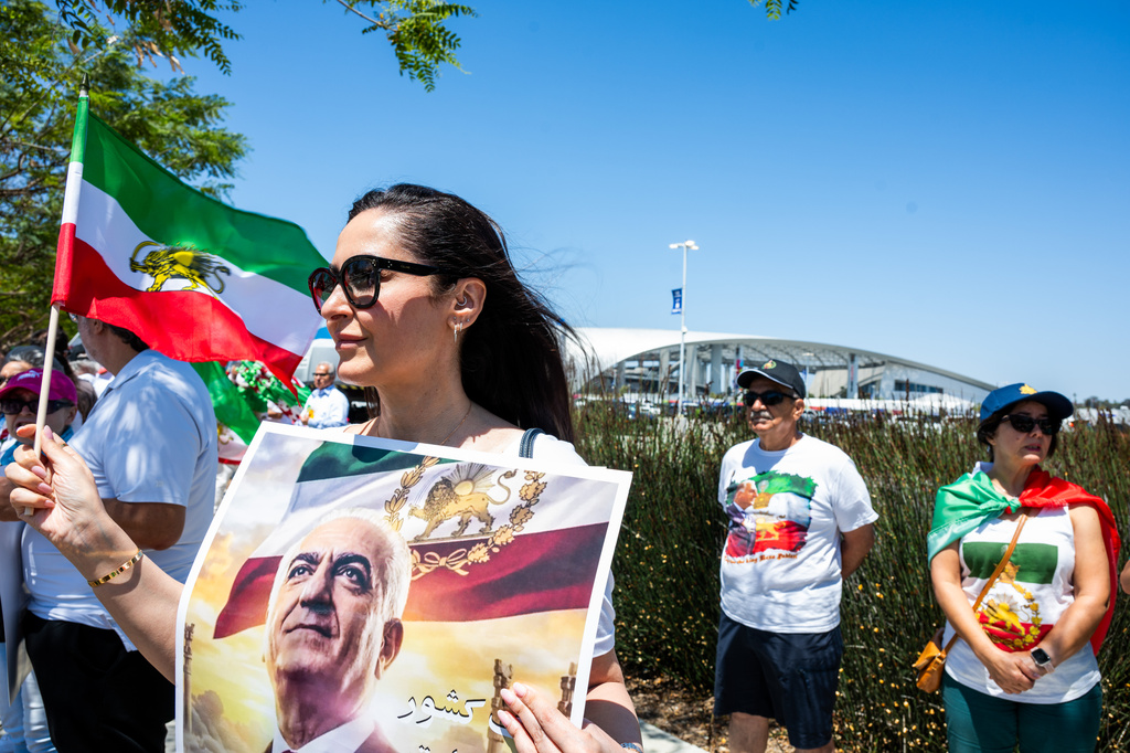 A woman holds a flag and poster during a protest in reaction to FIFA's ban of Iran's pre-revolutionary flag inside World Cup stadiums Sunday, June 7, 2026, in Inglewood, Calif. (AP Photo/Benjamin Hanson)