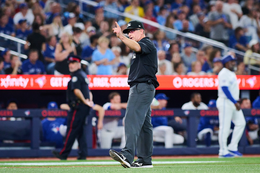 Umpire Chris Guccione, center, announces a rules check during an umpire review during the seventh inning of a baseball game between the Toronto Blue Jays and the Boston Red Sox in Toronto, Monday, Aug. 10, 2026. (Sammy Kogan/The Canadian Press via AP)