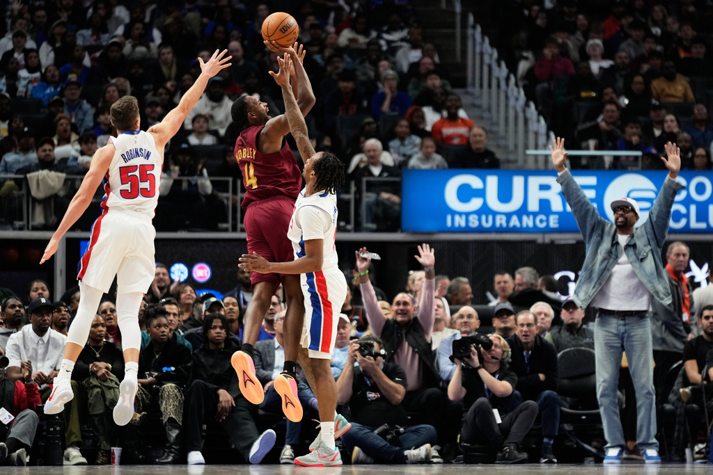 Cleveland Cavaliers center Evan Mobley, center, shoots against Detroit Pistons forward Duncan Robinson, left, and guard Ron Holland II, third from left, as former NBA player Jalen Rose, right, reacts during the first half of an NBA basketball game, Monday, Oct. 27, 2025, in Detroit. (AP Photo/Ryan Sun)